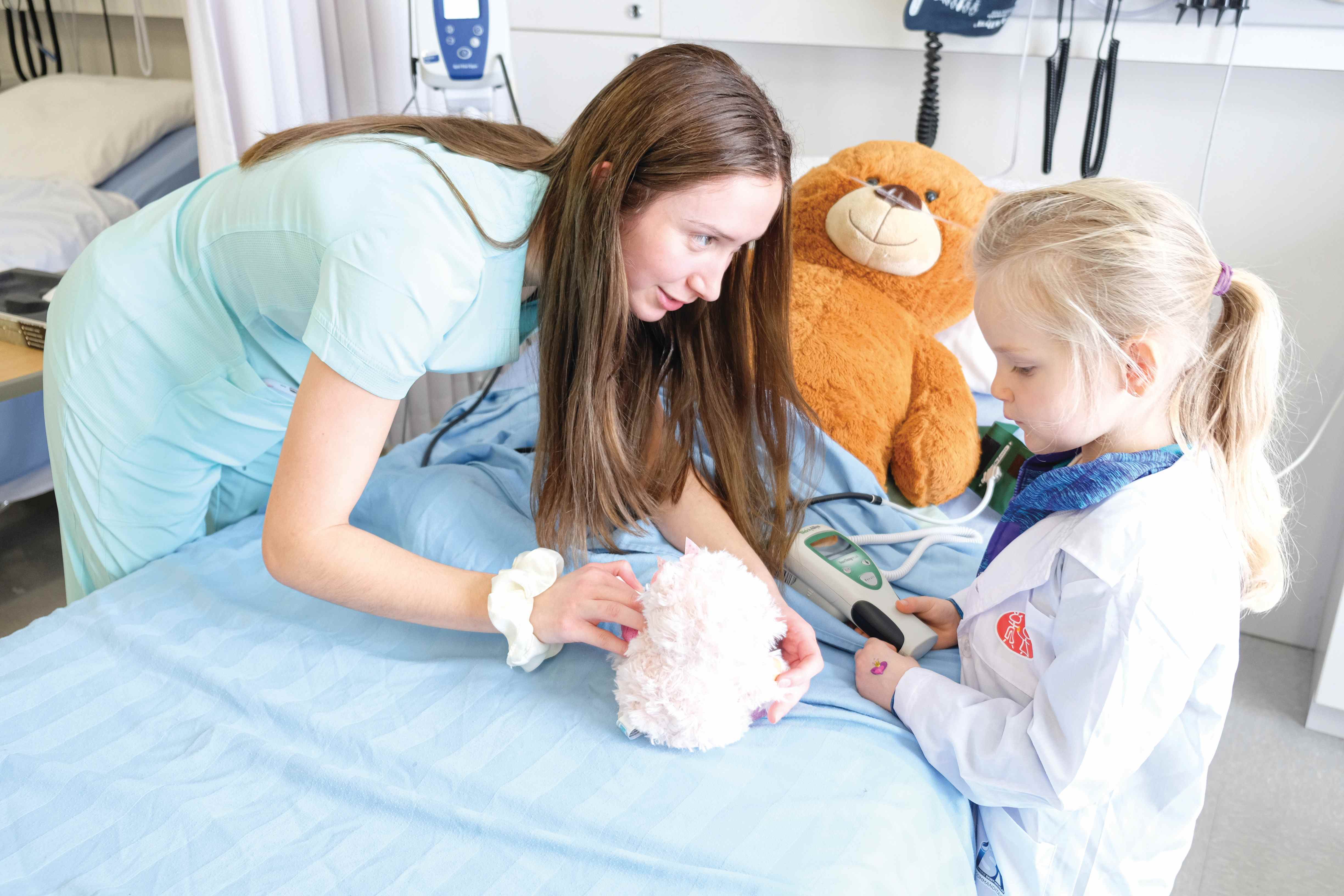 Une étudiante en soins infirmiers du Cégep de Lévis avec un enfant et un ourson en peluche autour d'un lit d'hôpital.